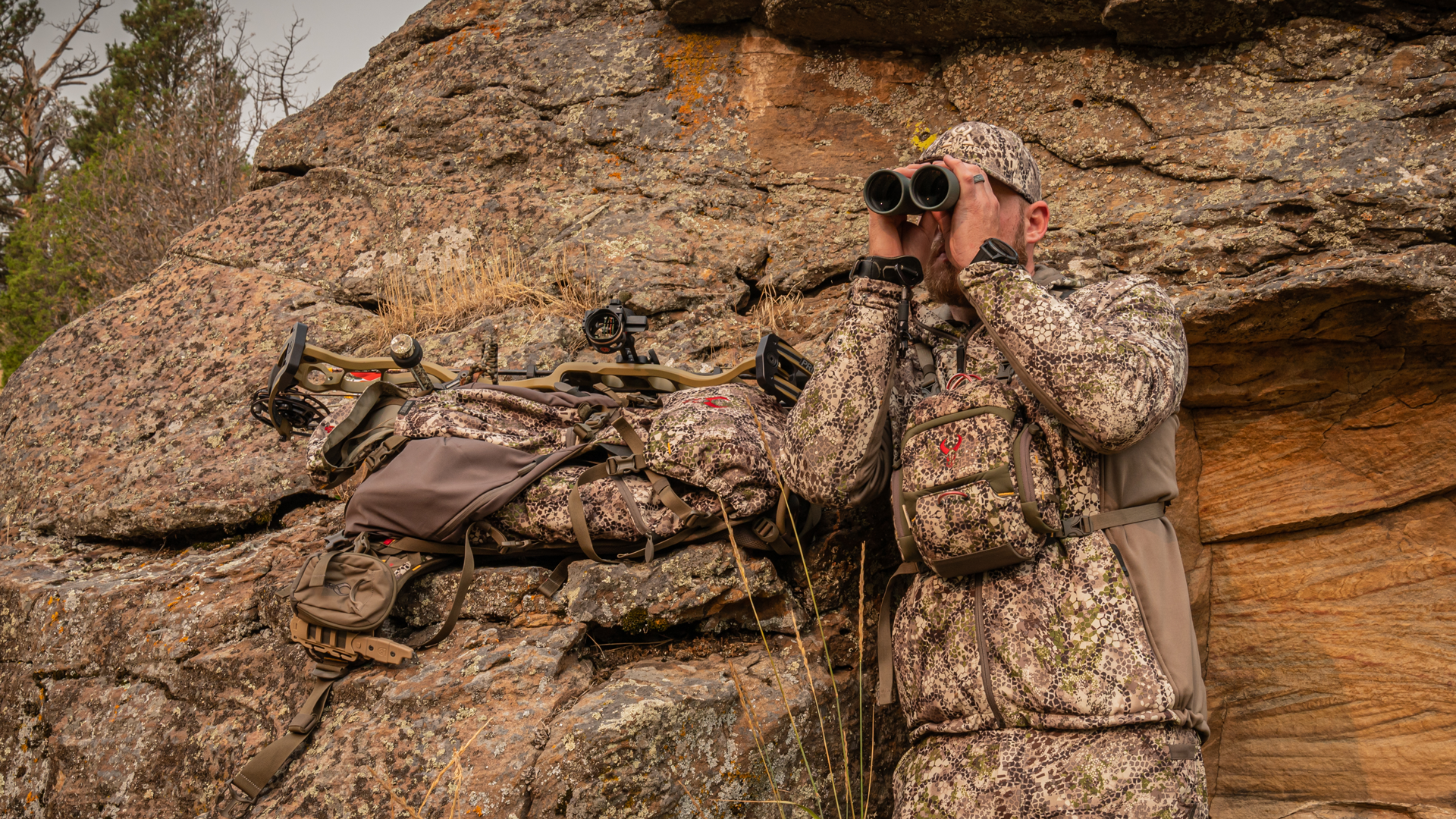 male hunter blending into surroundings in camo, using binoculars