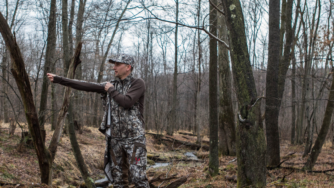 man putting on hunting jacket in the forest