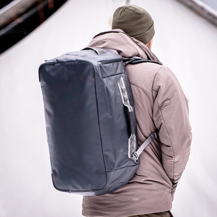 Person wearing a large Badlands backpack with logo, dressed for cold weather. Neutral background for clear product focus.
