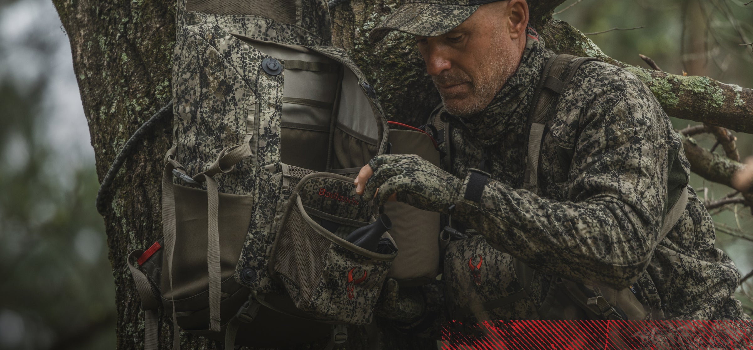 Hunter in Badlands camo gear accesses a Badlands backpack with logo, organizing equipment in a forested setting.