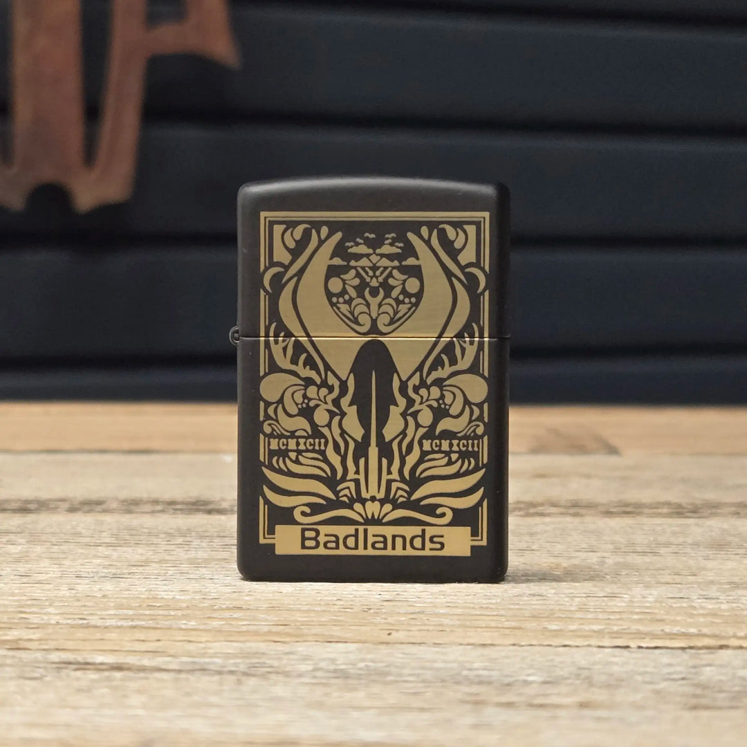 Black lighter with gold Badlands logo skull and antlers, ornate design, and "Badlands" text on a wooden surface.