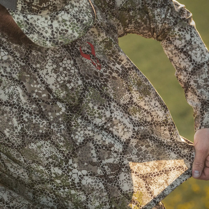 Person wearing Badlands camo shirt with red Badlands skull logo, holding fabric to show texture and pattern.
