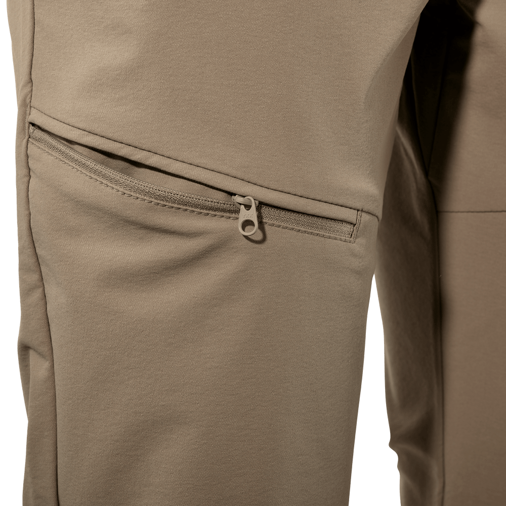 Close-up of tan Badlands pants showing a zippered thigh pocket with subtle Badlands skull logo on the zipper pull.