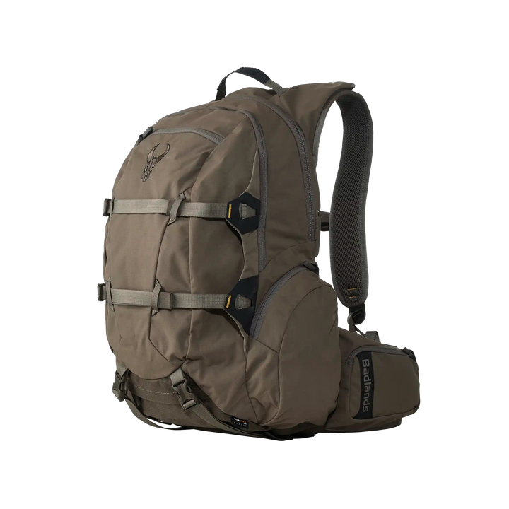 Tan Badlands backpack with skull logo, multiple compartments, padded straps, and side pocket. Designed for outdoor use.
