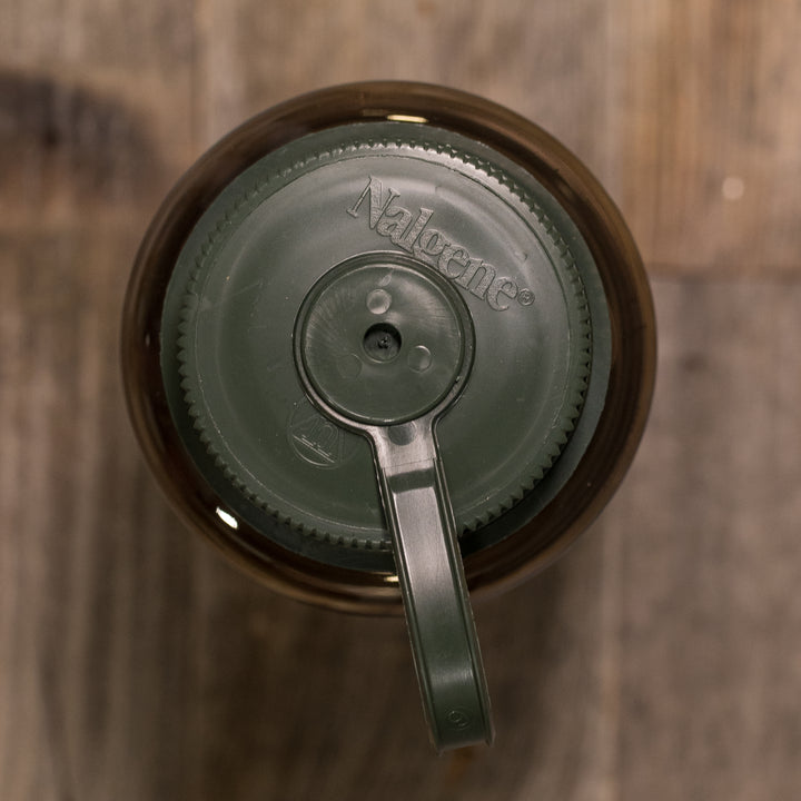 Top view of a green Nalgene bottle lid on a wood surface, featuring the Badlands skull logo.