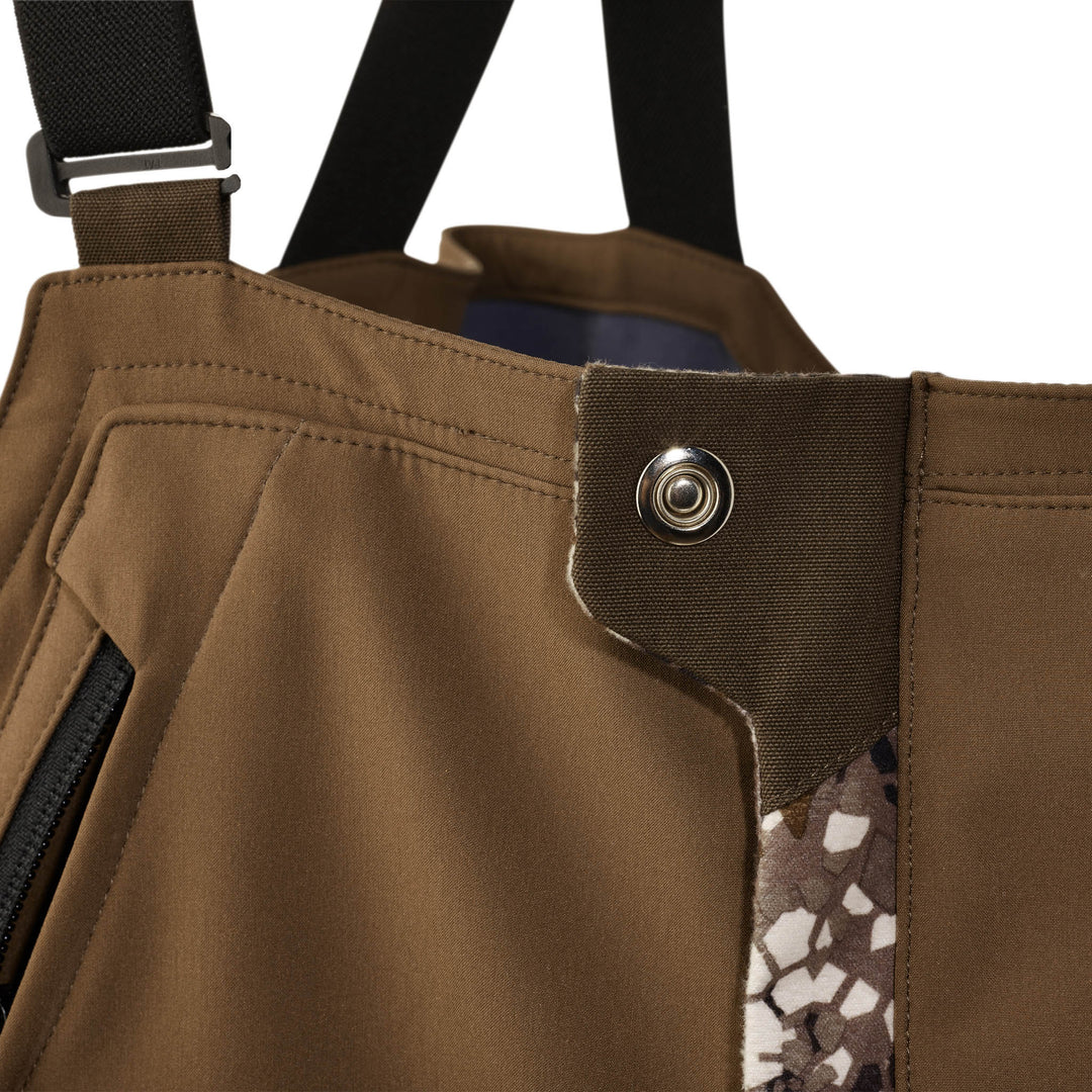 Close-up of Badlands hunting bib waist with snap closure, camo accent, and black suspender strap.
