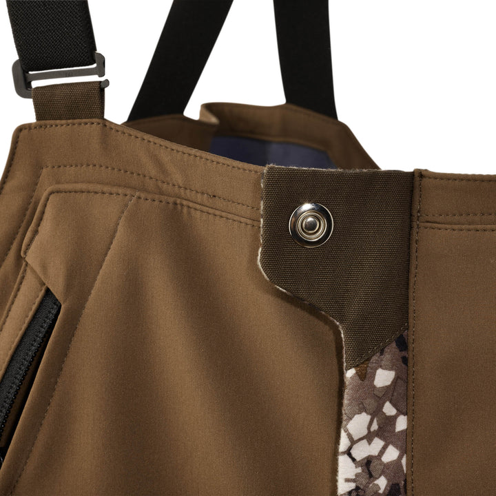 Close-up of Badlands hunting bib waist with snap closure, camo accent, and black suspender strap.
