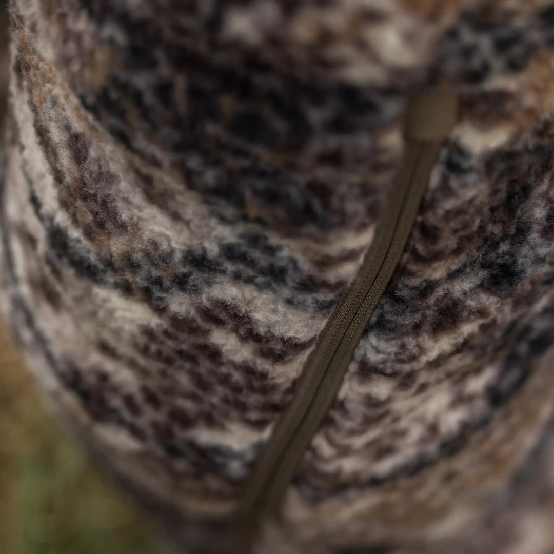 Close-up of Badlands camo fleece fabric with a brown zipper, showing soft texture and natural earth-tone pattern.
