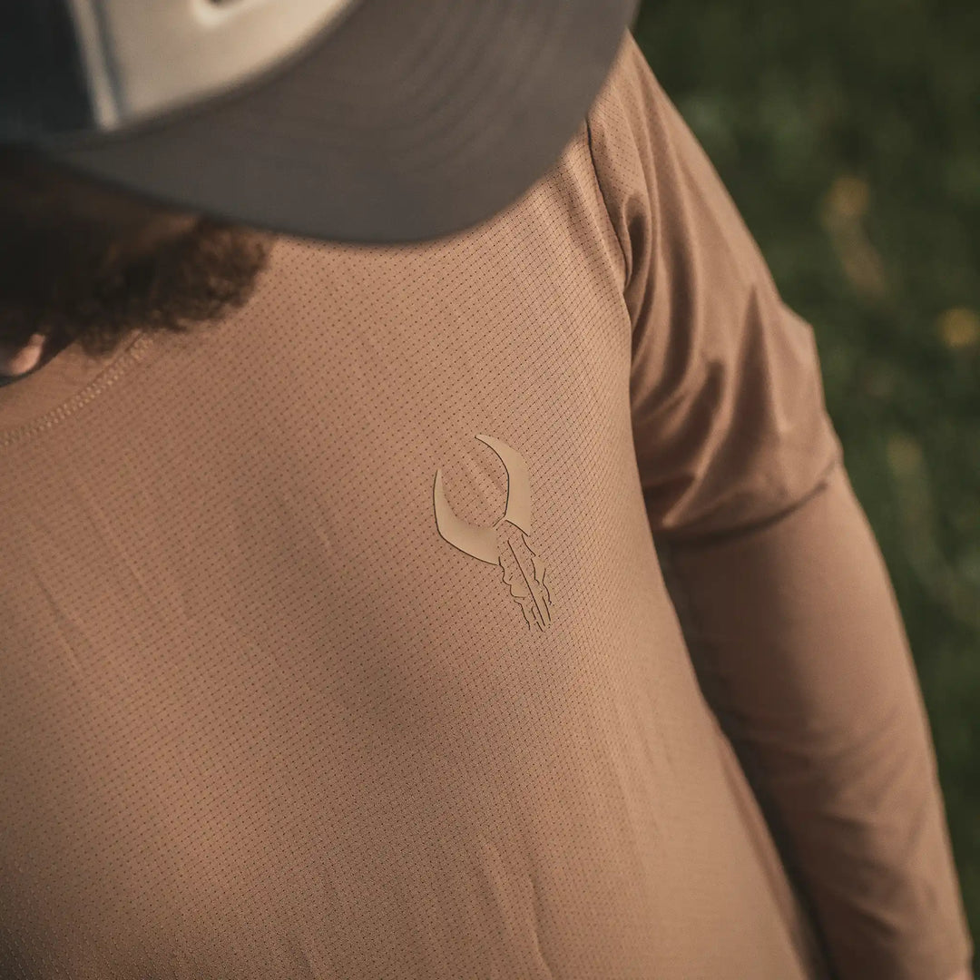 Man wearing a tan Badlands shirt with the Badlands skull logo on the chest, outdoors in natural light.