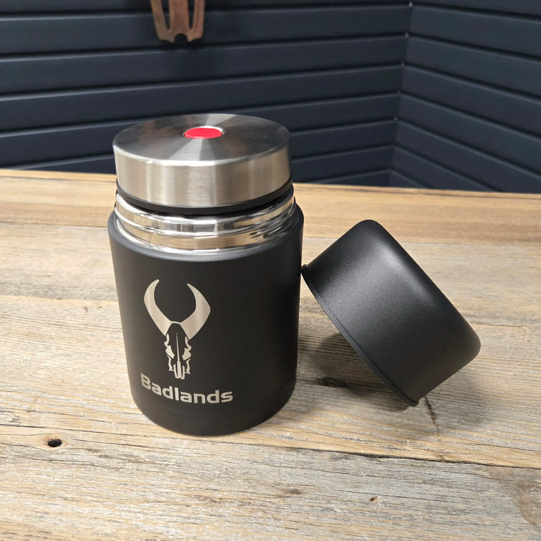 Black Badlands thermos with skull logo on wood table; lid off, stainless steel top visible.