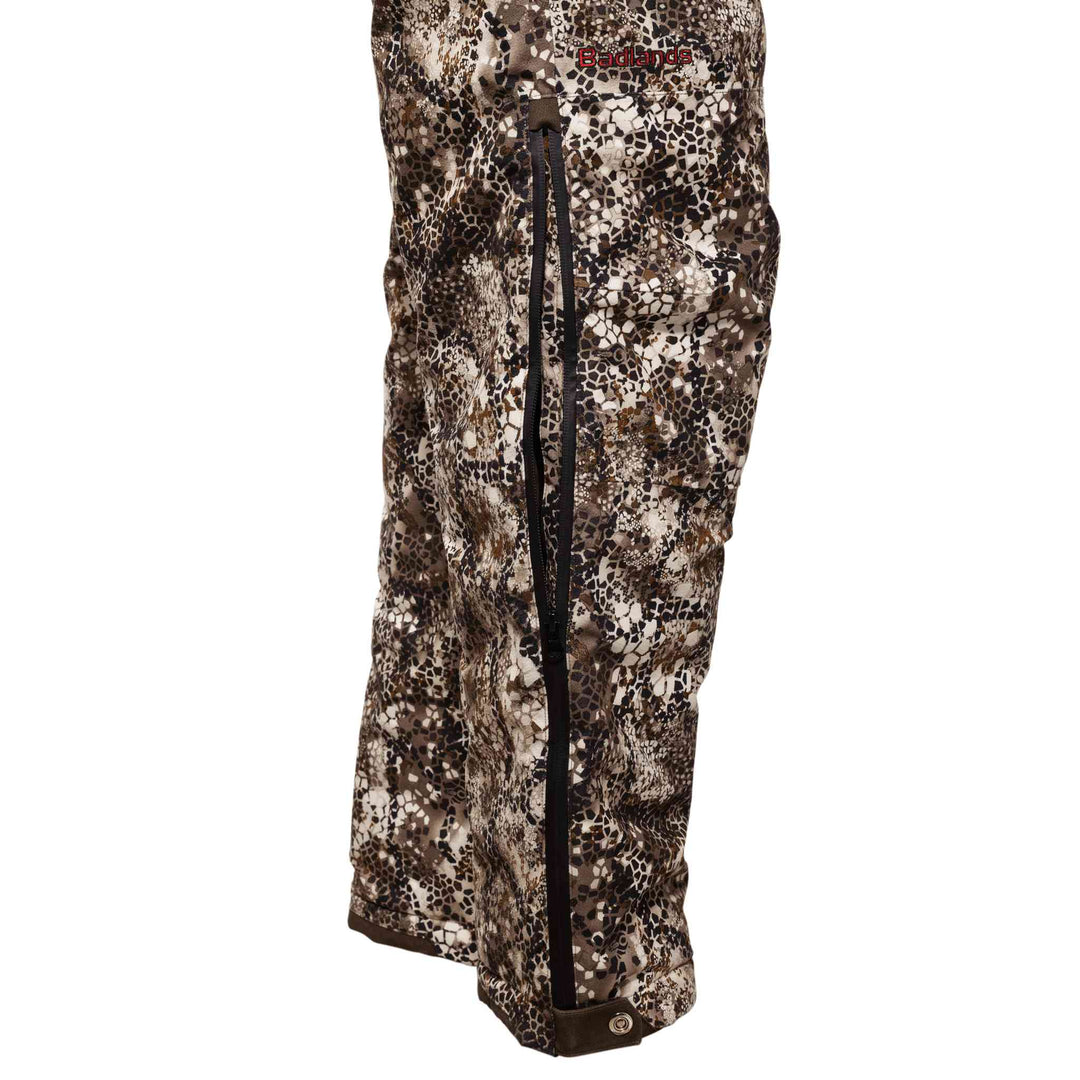 Badlands camo rain pants with side zipper, featuring the Badlands skull logo near the waist.