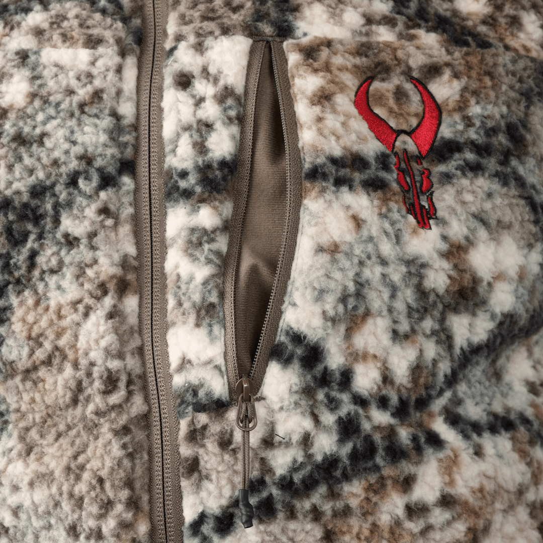 Close-up of a camo-patterned Badlands fleece jacket with a red skull logo and a vertical zippered chest pocket.