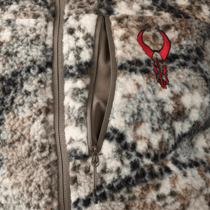 Close-up of a camo-patterned Badlands fleece jacket with a red skull logo and a vertical zippered chest pocket.
