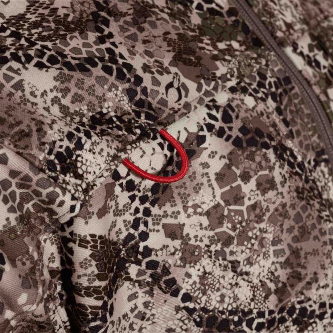 Close-up of Badlands camo fabric with a red Badlands skull logo loop on a zippered pocket.