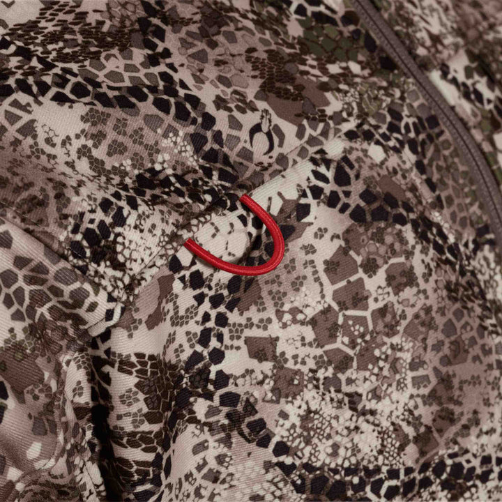 Close-up of Badlands camo fabric with a red Badlands skull logo loop on a zippered pocket.