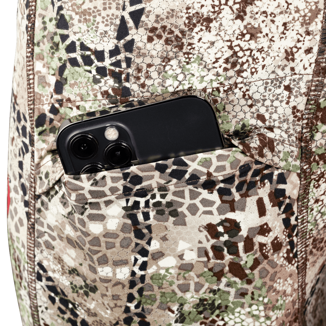 Close-up of a Badlands camo pocket holding a smartphone; Badlands skull logo visible on the fabric.