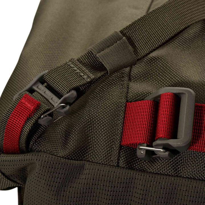 Close-up of a Badlands backpack strap with red webbing, buckle, and skull logo; durable fabric for outdoor use.
