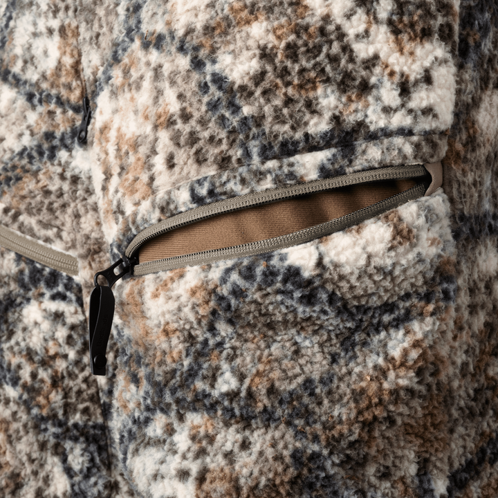 Close-up of Badlands camo fleece jacket with zippered pocket; soft texture and earth-tone pattern for outdoor use.