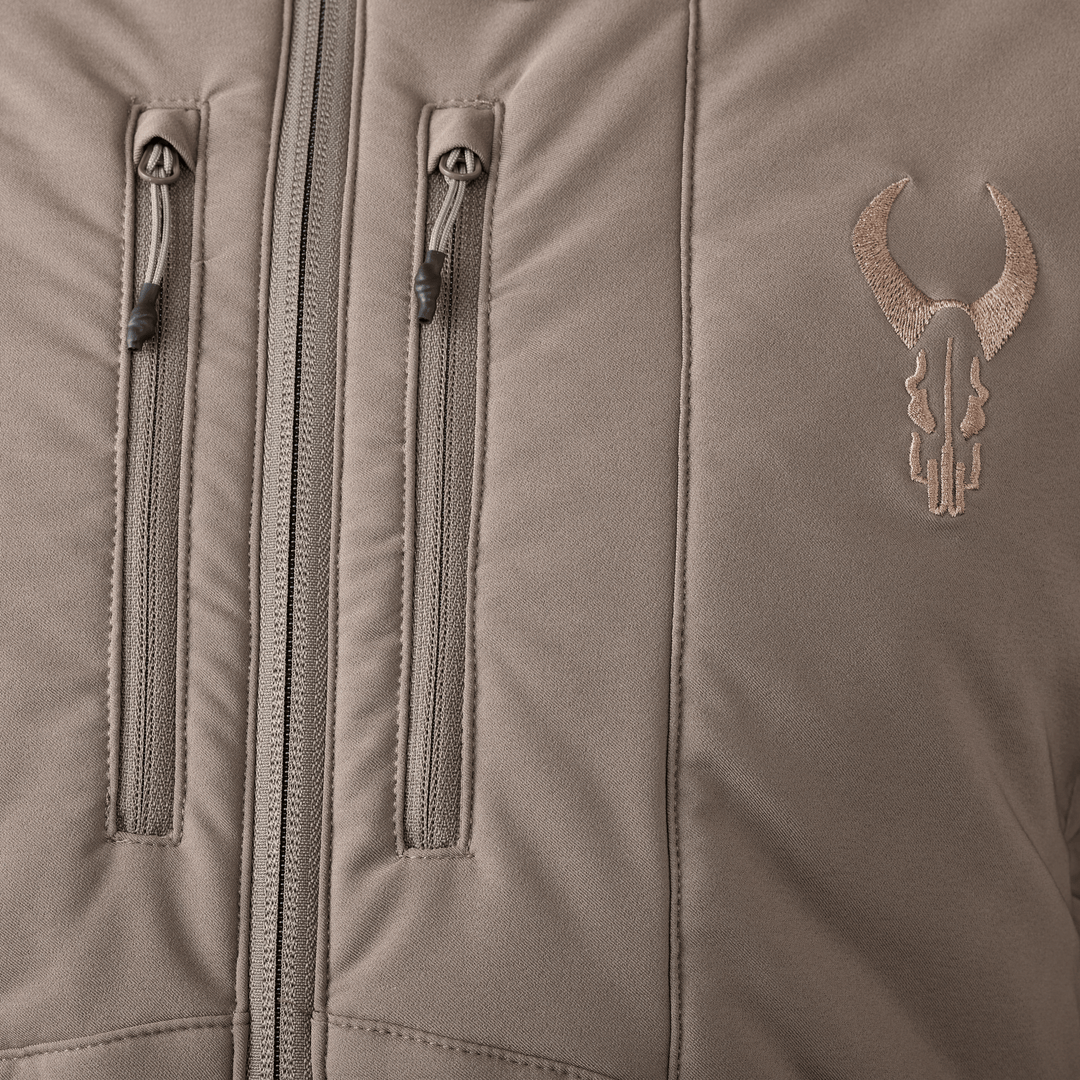 Close-up of a tan Badlands jacket with two vertical chest zippers and an embroidered Badlands skull logo on the right side.