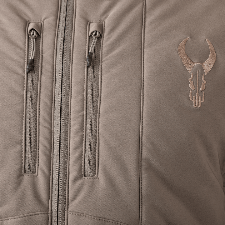 Close-up of a tan Badlands jacket with two vertical chest zippers and an embroidered Badlands skull logo on the right side.