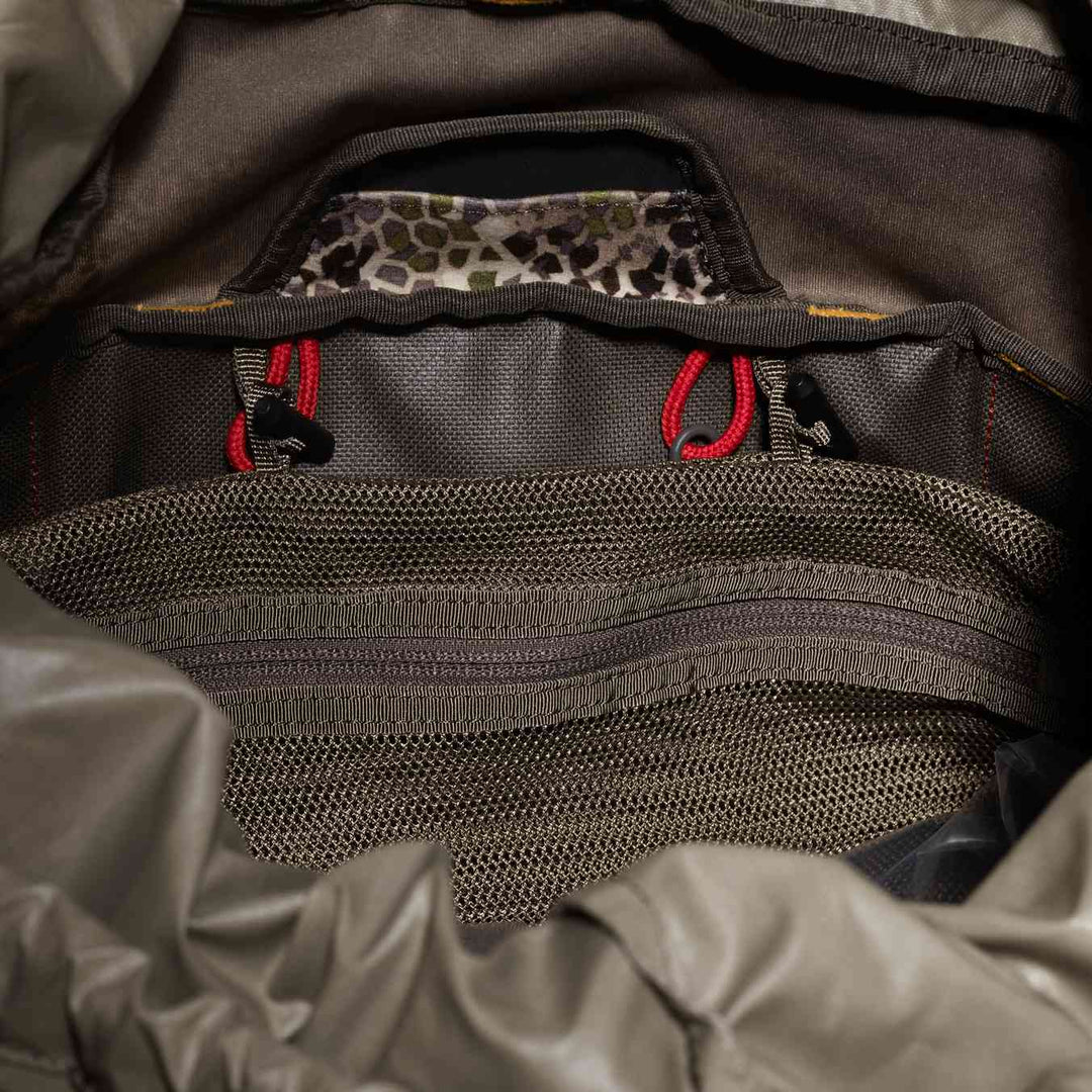 Interior of a Badlands backpack showing mesh pocket, red drawstrings, and the Badlands skull logo on camo fabric.