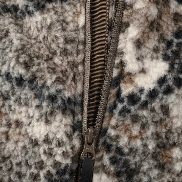 Close-up of Badlands camo fleece fabric with a brown zipper, showing texture and detail for outdoor apparel.