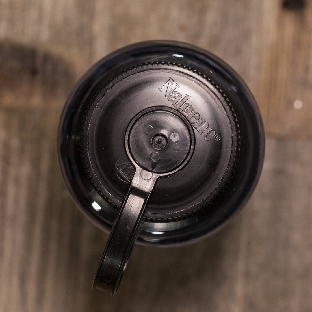 Black Nalgene bottle lid with handle, viewed from above, on a wood surface. No Badlands logo visible.