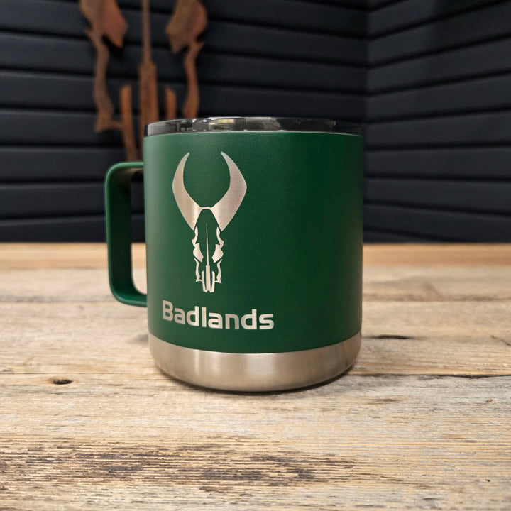 Green Badlands mug with silver skull logo on wood table, designed for outdoor use; ADA-friendly contrast and branding.