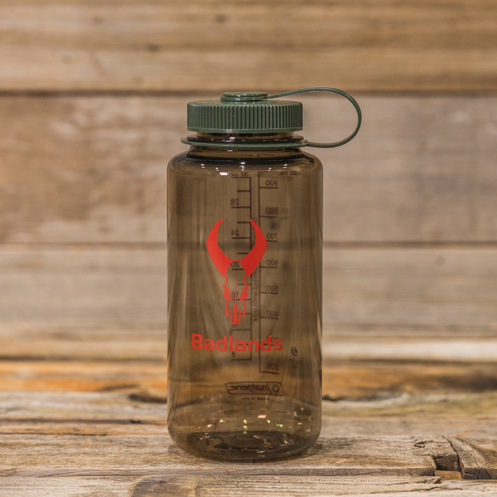 Smoky water bottle with green lid, red Badlands logo (skull), and measurement markings; sits on rustic wood background.