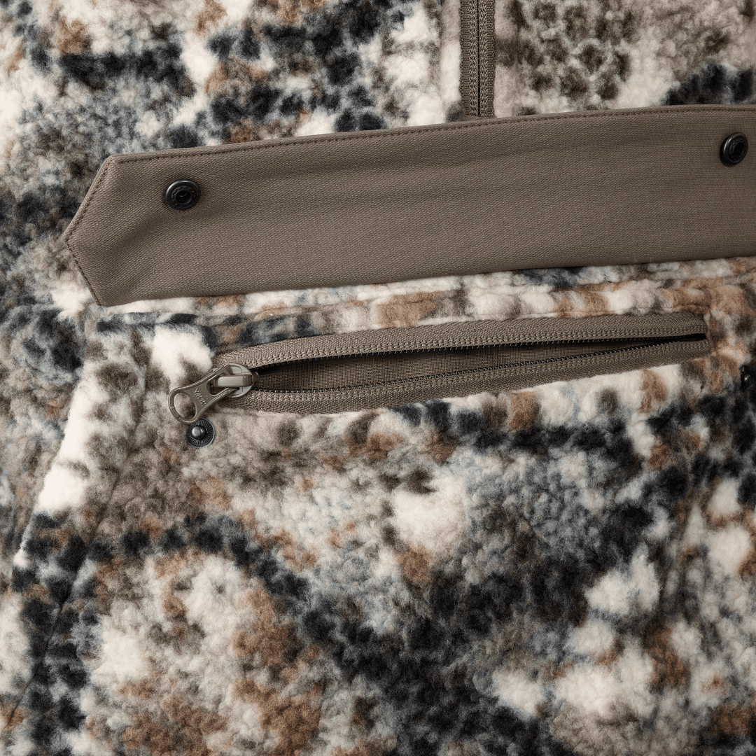 Close-up of Badlands camo fleece fabric with zippered pocket and snap flap; skull logo zipper pull visible.