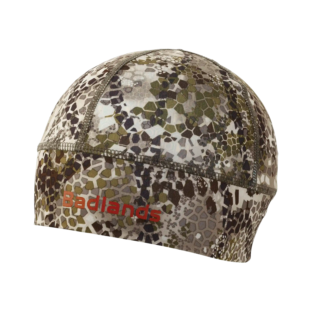 Camo skull cap with Badlands logo in red; lightweight, fitted design for outdoor use.