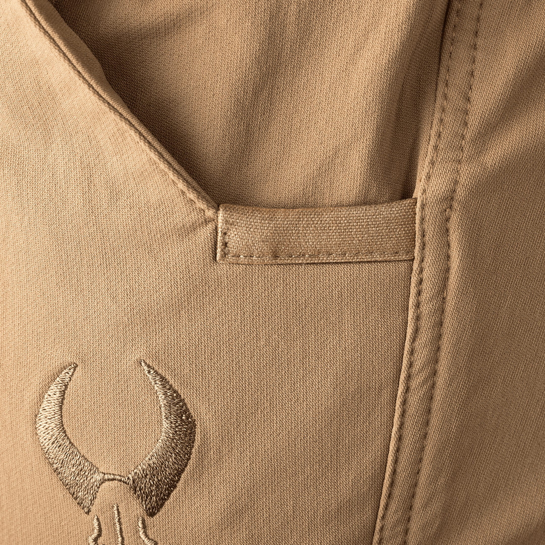 Close-up of tan fabric pocket with embroidered Badlands skull logo below the opening.