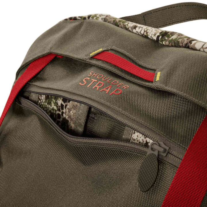 Close-up of a Badlands backpack pocket labeled "Shoulder Strap," featuring red accents and camo fabric detail.