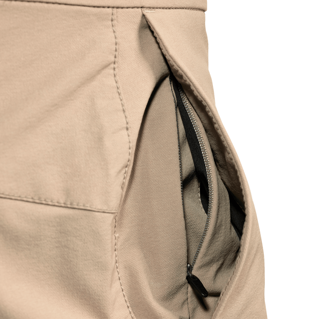 Close-up of a tan Badlands pant pocket with an inner zippered compartment for secure storage. No visible logo.