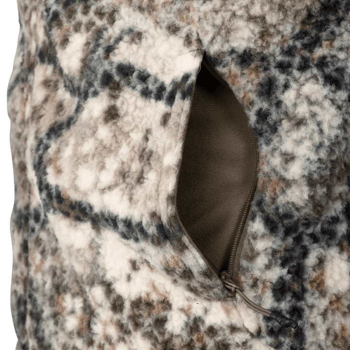 Close-up of a Badlands camo fleece jacket pocket with a zipper, showing soft textured fabric and subtle Badlands skull logo.