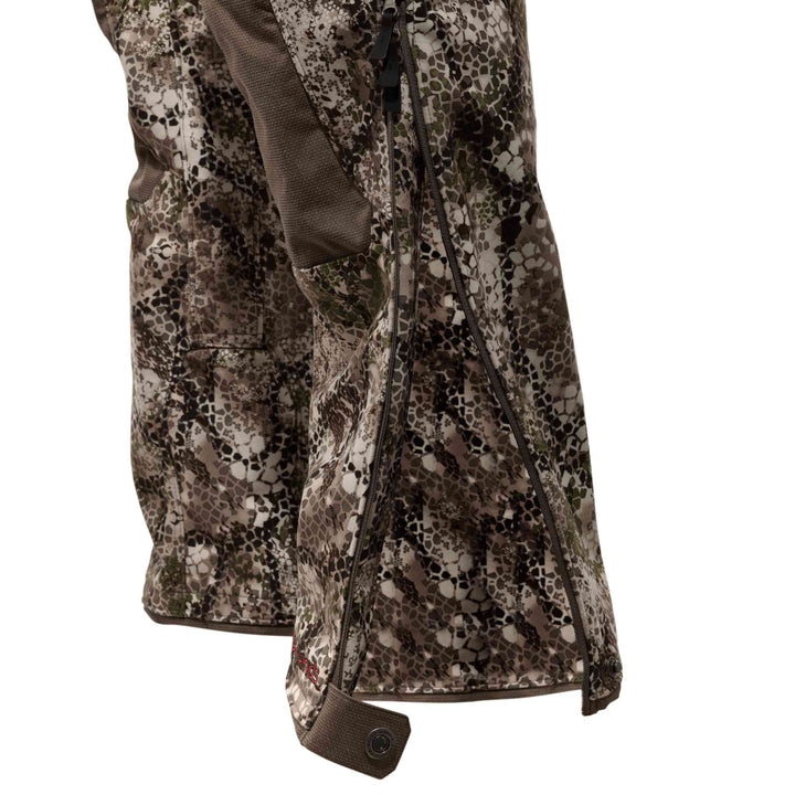 Close-up of Badlands camo pants with side zipper and snap closure; Badlands skull logo visible near the hem.
