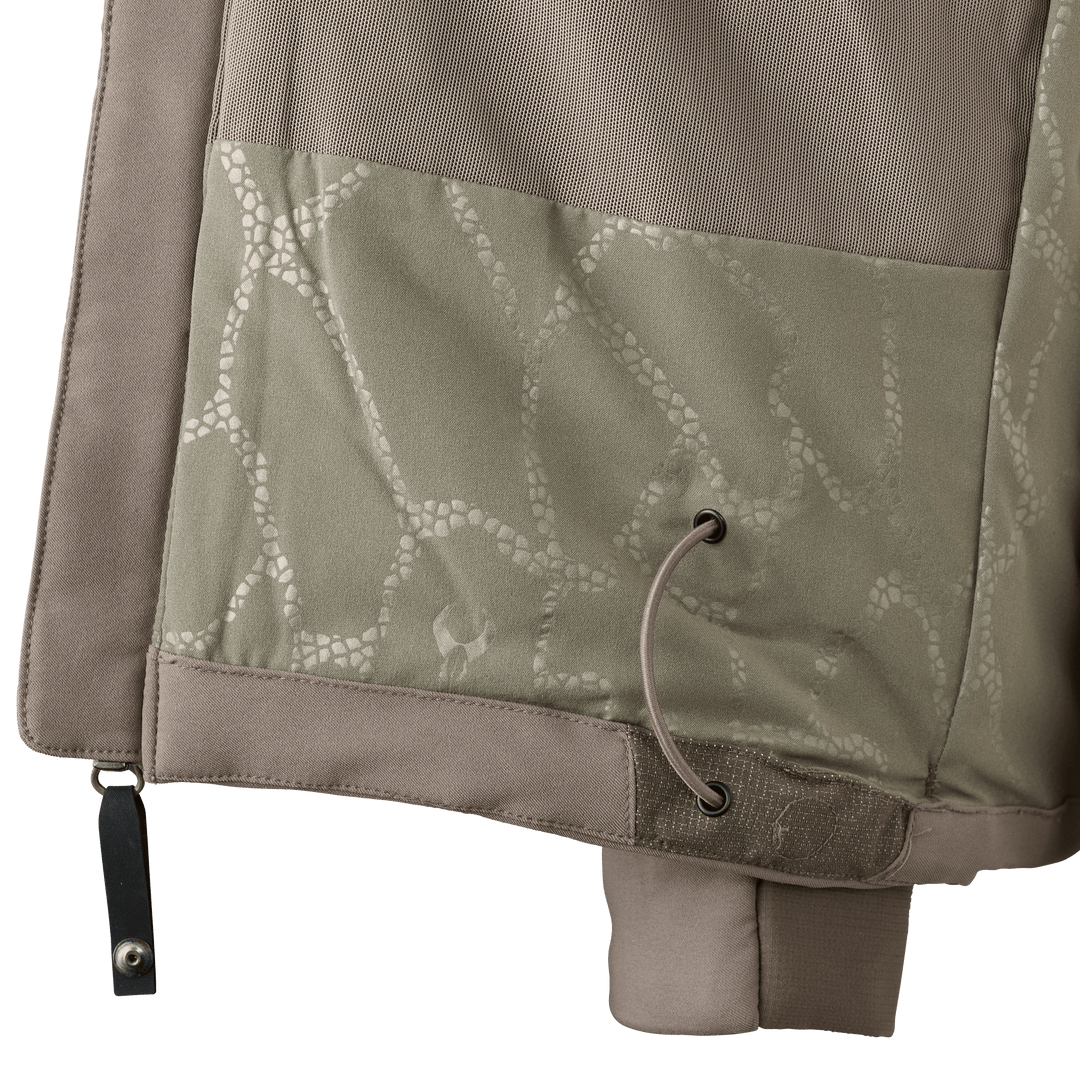 Close-up of a Badlands jacket hem with drawcord, camo pattern, and subtle Badlands skull logo.