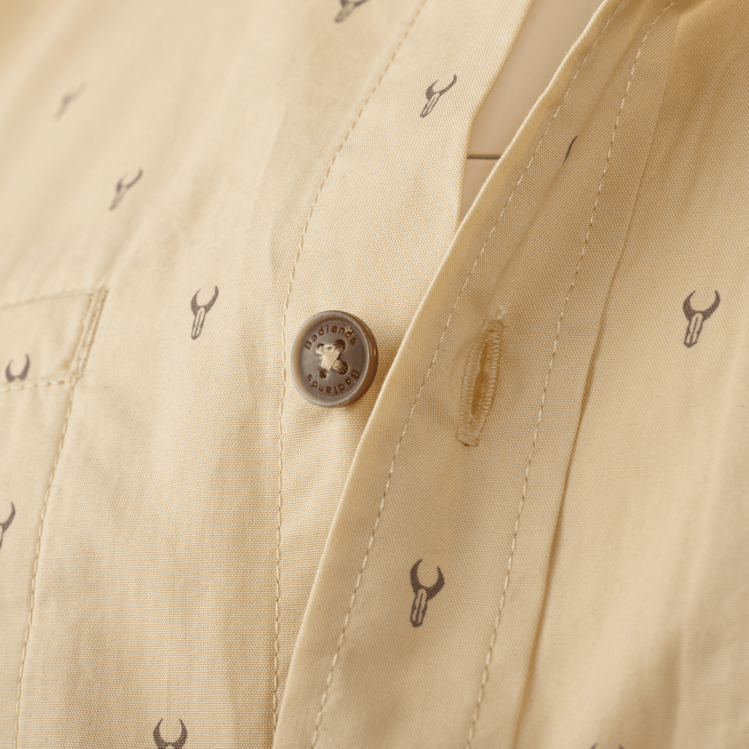 Close-up of tan Badlands shirt with logo skull print and branded button for accessible identification.