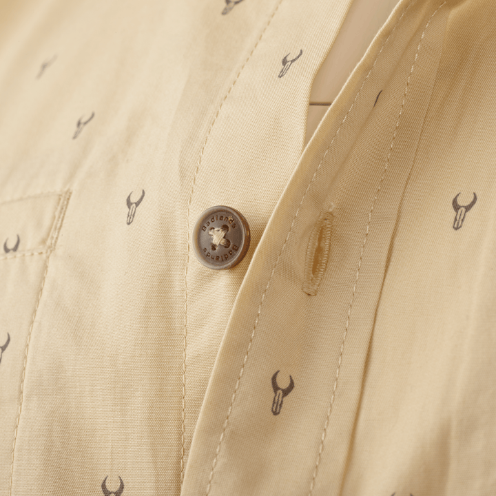 Close-up of tan Badlands shirt with logo skull print and branded button for accessible identification.