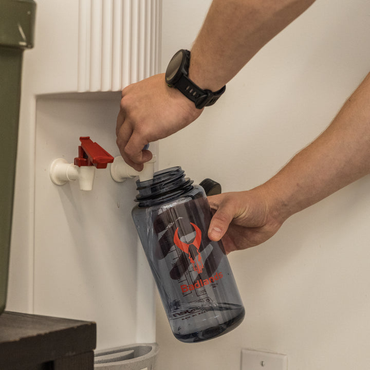 Person filling a Badlands water bottle, featuring the skull logo, from a white water dispenser.