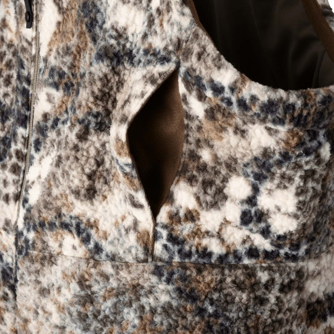 Close-up of Badlands camo fleece vest with zip and pocket; textured fabric in brown, blue, and white pattern.