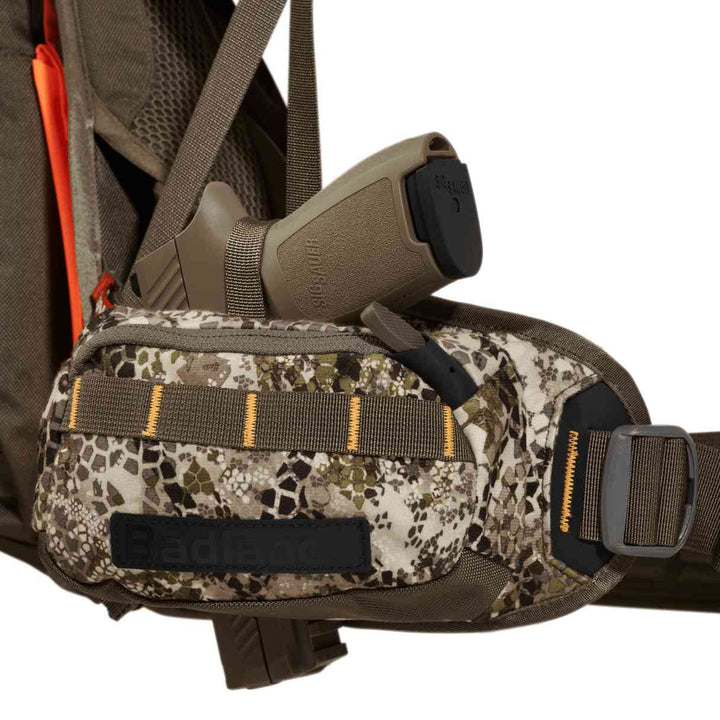 Badlands camo hip belt pouch with holstered handgun and Badlands skull logo, attached to a hunting backpack.