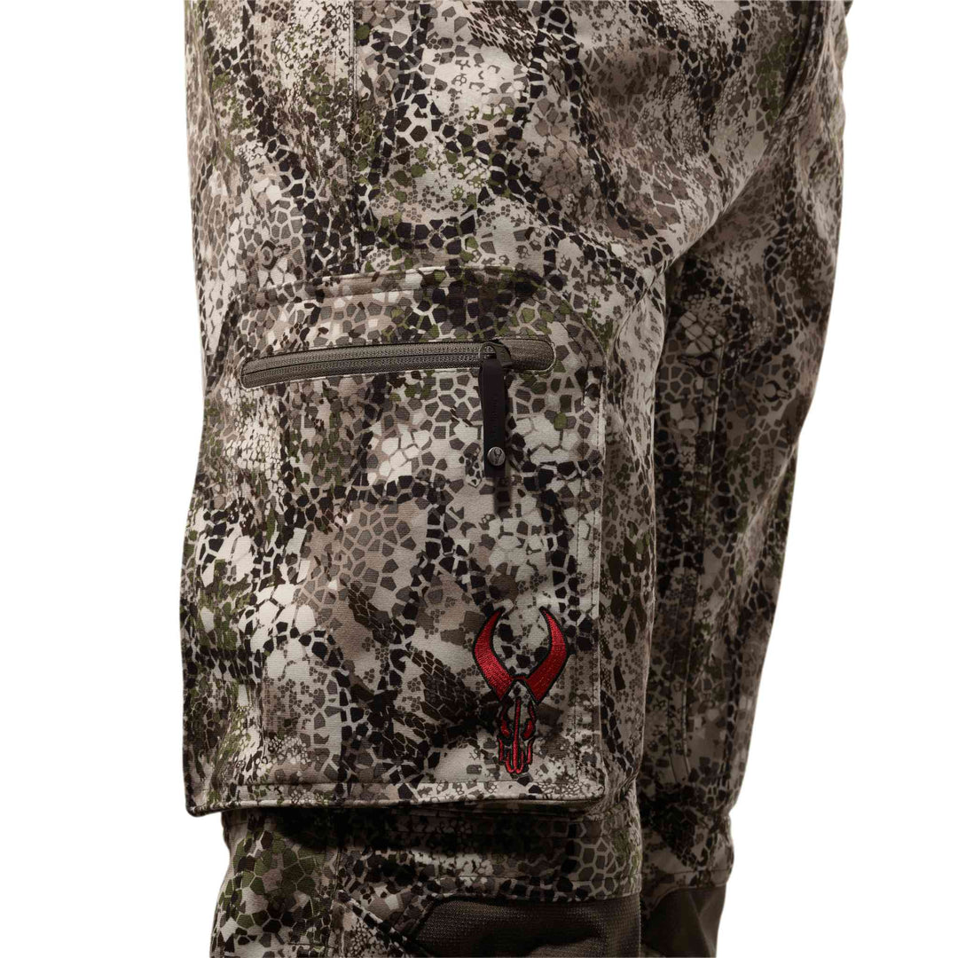 Close-up of Badlands camo pants with a zippered pocket and red Badlands skull logo on the thigh.