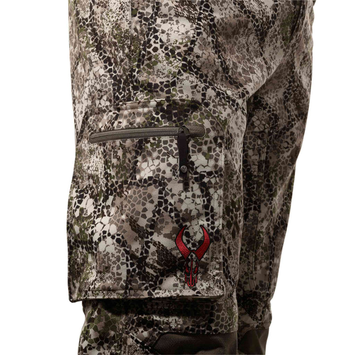 Close-up of Badlands camo pants with a zippered pocket and red Badlands skull logo on the thigh.