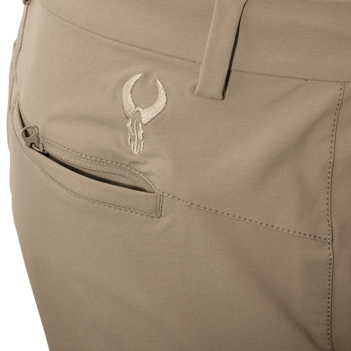 Close-up of tan Badlands pants pocket with embroidered skull logo and a zippered pocket for secure storage.