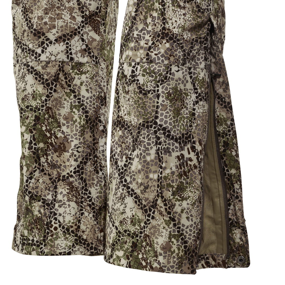 Close-up of Badlands camo rain pants with side zipper open, showing waterproof material and detailed camouflage pattern.