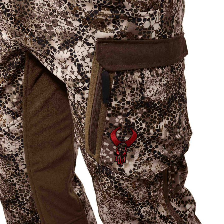 Close-up of Badlands camo pants with red skull logo, zippered pocket, and reinforced knee panel.