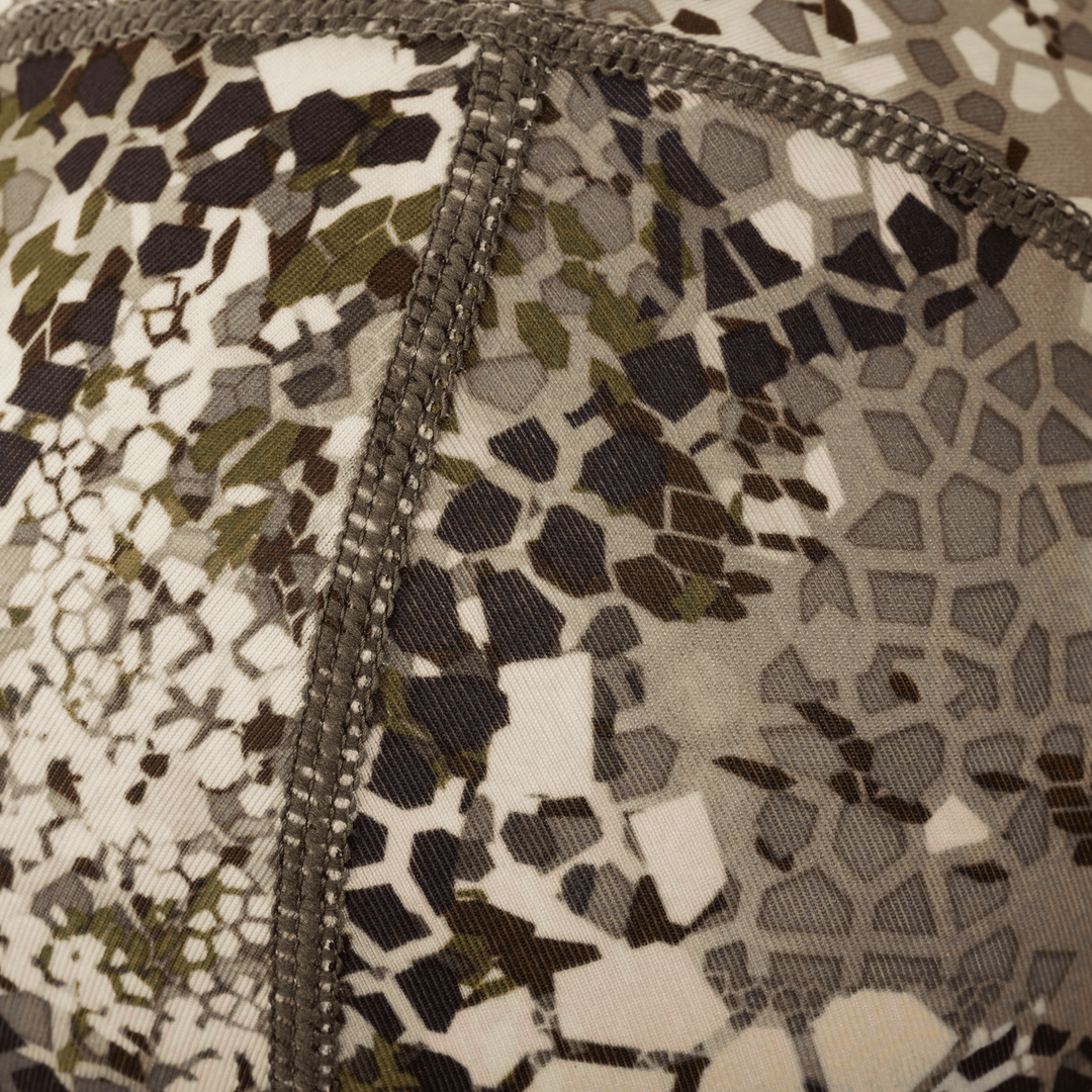 Close-up of Badlands camo fabric with reinforced stitching; abstract skull logo pattern visible in muted earth tones.