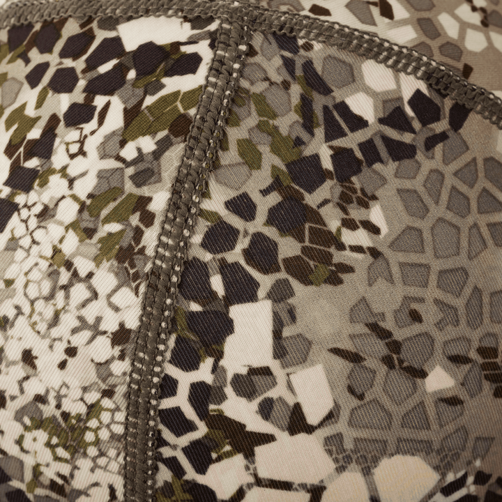 Close-up of Badlands camo fabric with reinforced stitching; abstract skull logo pattern visible in muted earth tones.