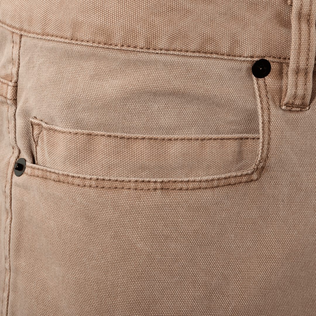 Close-up of tan Badlands pants pocket; metal rivet features the Badlands skull logo for brand identification.